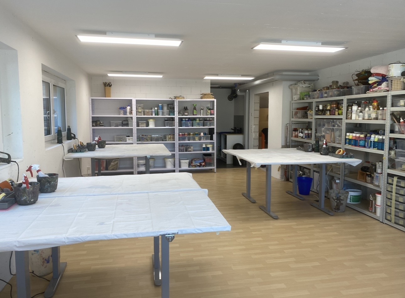 Helles Atelier Coni-Art mit grossen Arbeitstischen und Regalen voller Farben und Materialien